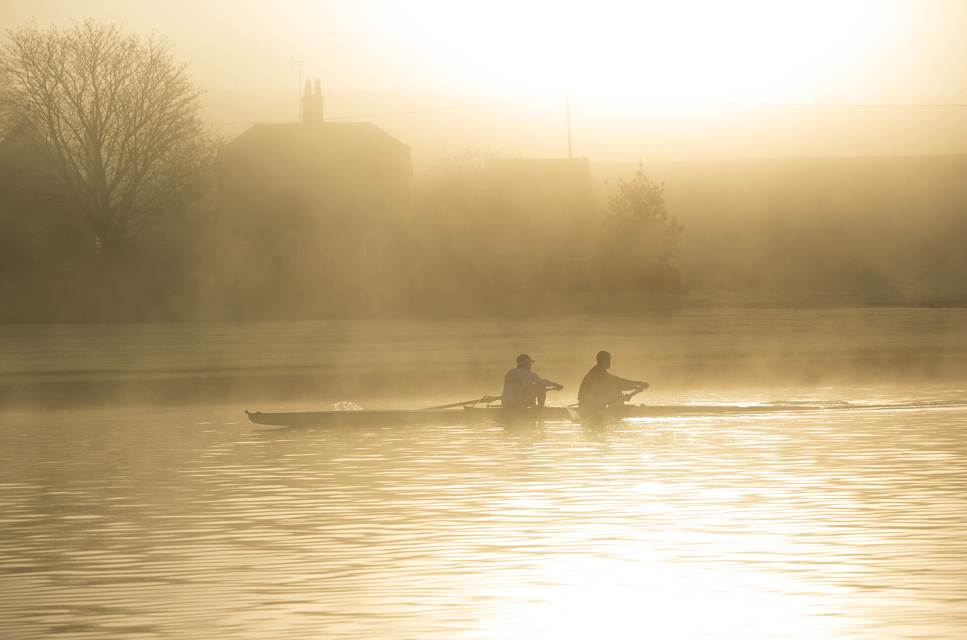 Two rowers silhouetted in the hazy early morning mists on the River Thames