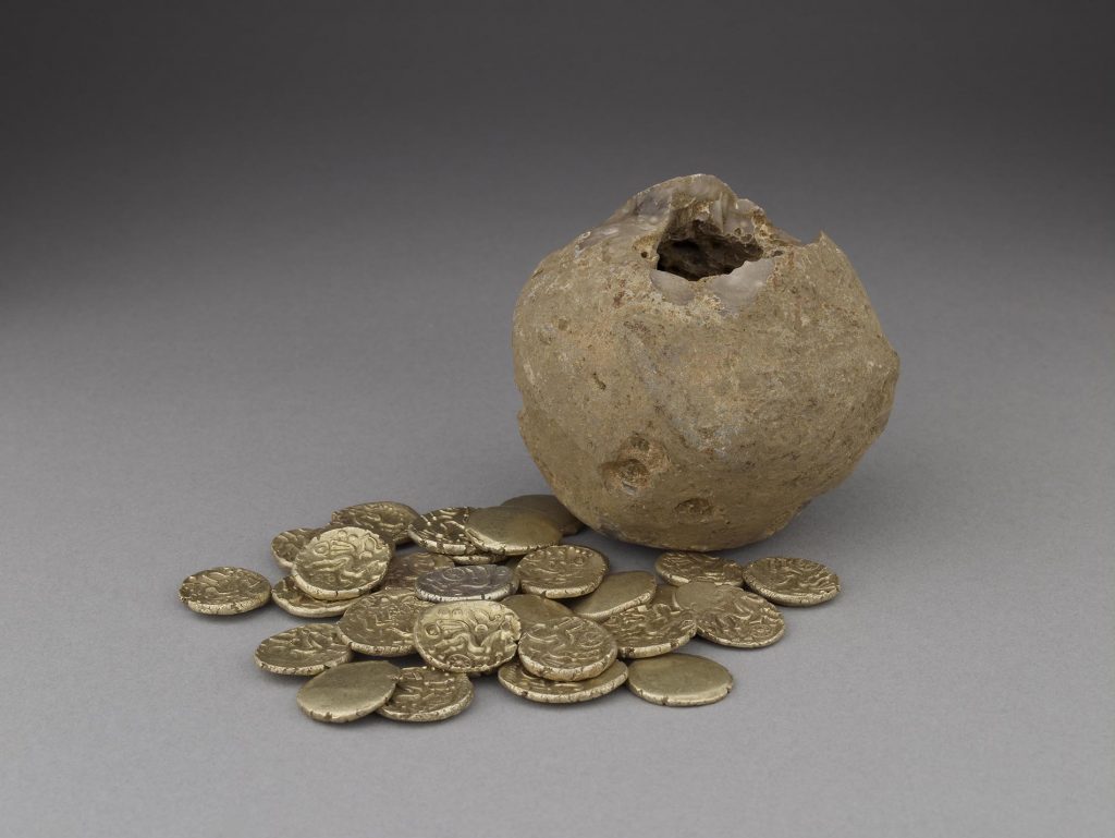 A hollow ball of flint at the foot of which are an array of gold coins with a stylist image of a horse stamped onto them.