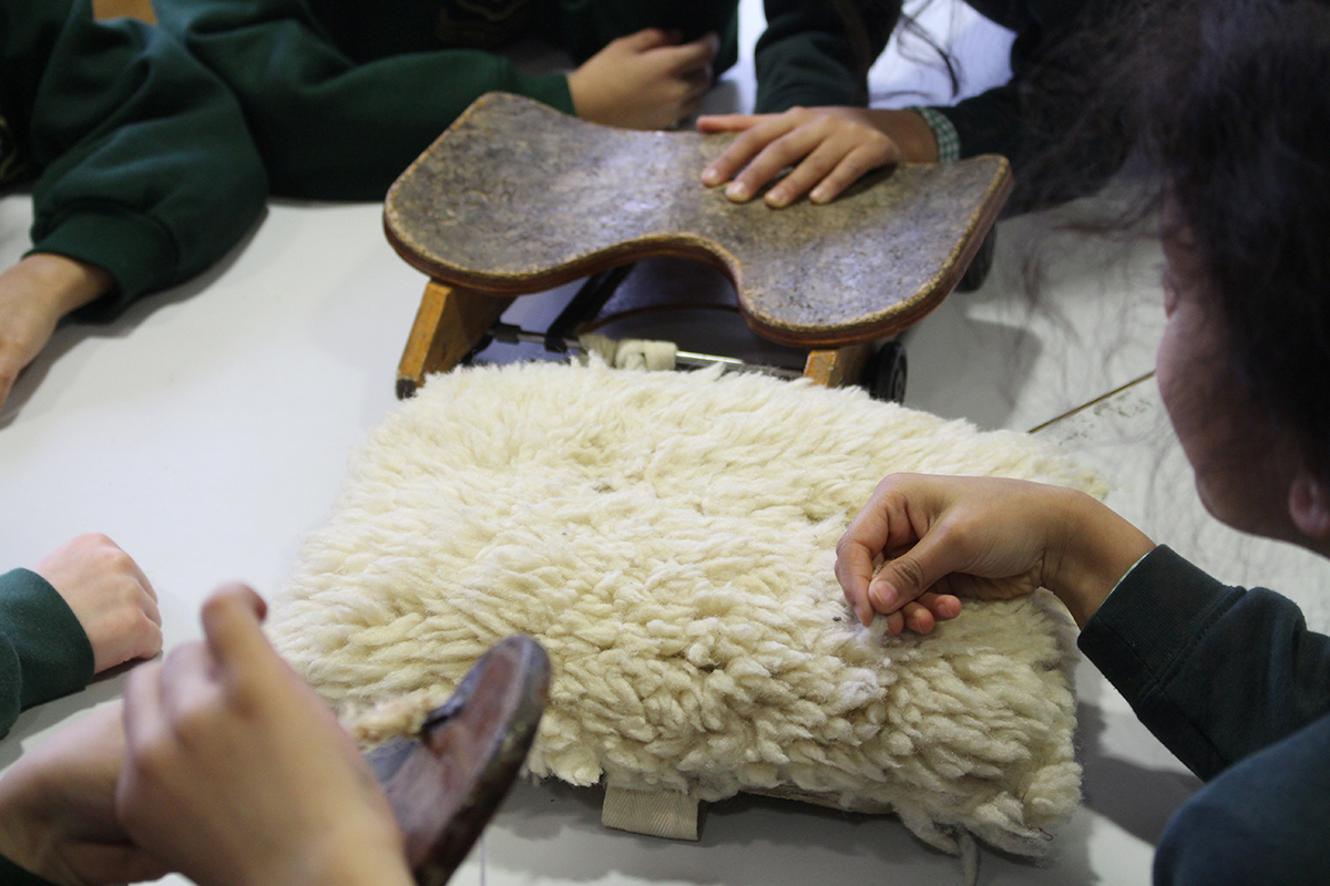 Children in school uniform feel different materials including a sheep's fleece seat cushion and a wooden sliding seat from a rowing boat
