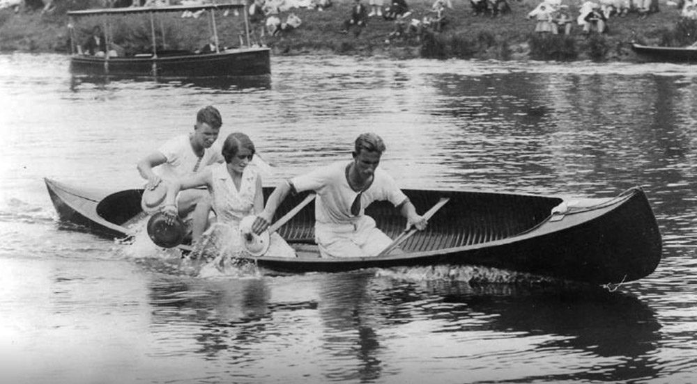 Two men and a woman using tin plates to row a canoe in the 1930s