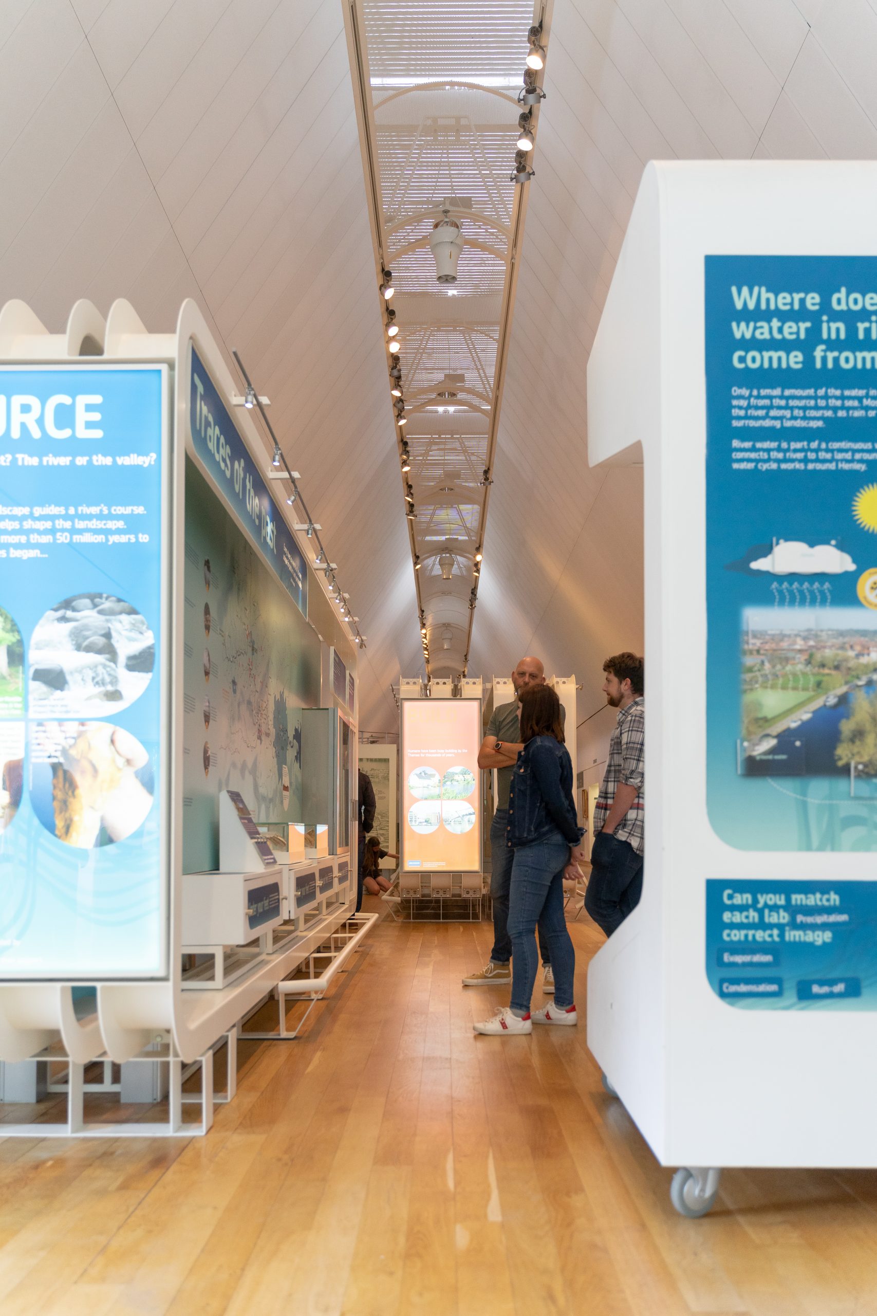 A woman and two men are looking at a large map display in a gallery, seen from between blue and white displays about water..