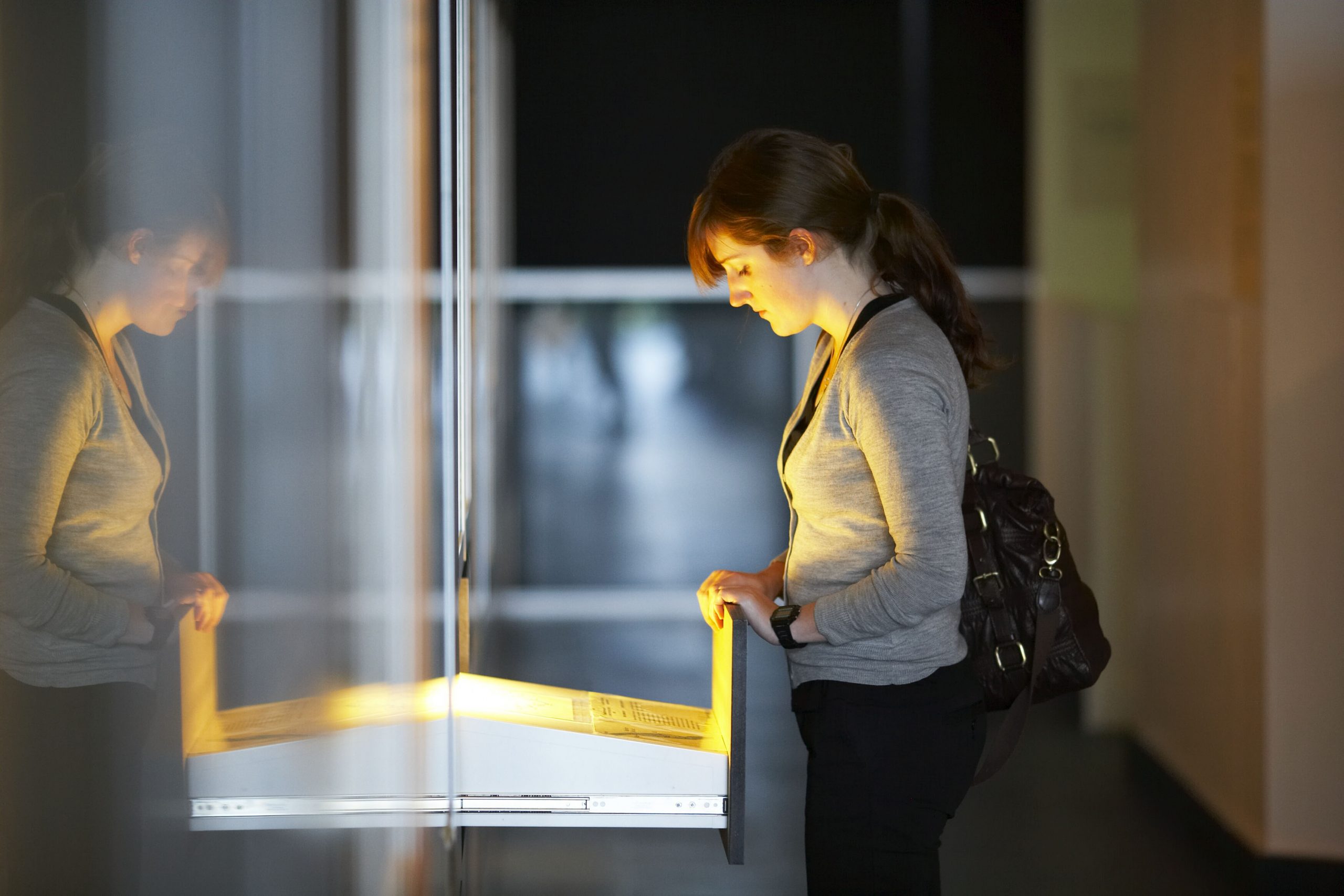 A young woman is illuminated with a warm glow from a display in an open drawer that she is looking at.